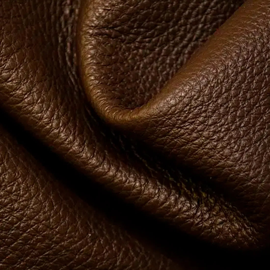 A close-up of draped brown pebbled leather showing its rich texture and grain.