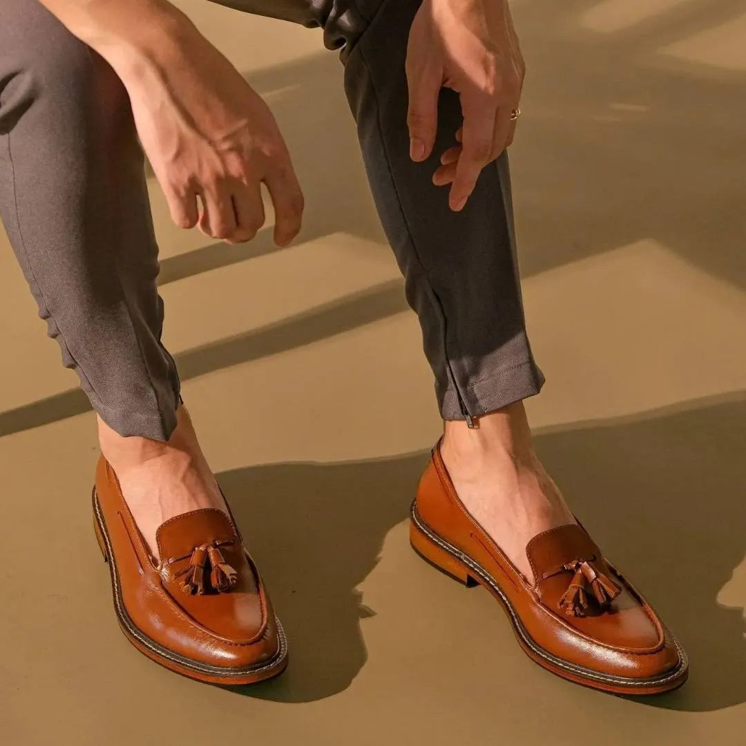 Brown loafers with tassels worn by a person on a beige surface
#color_tan