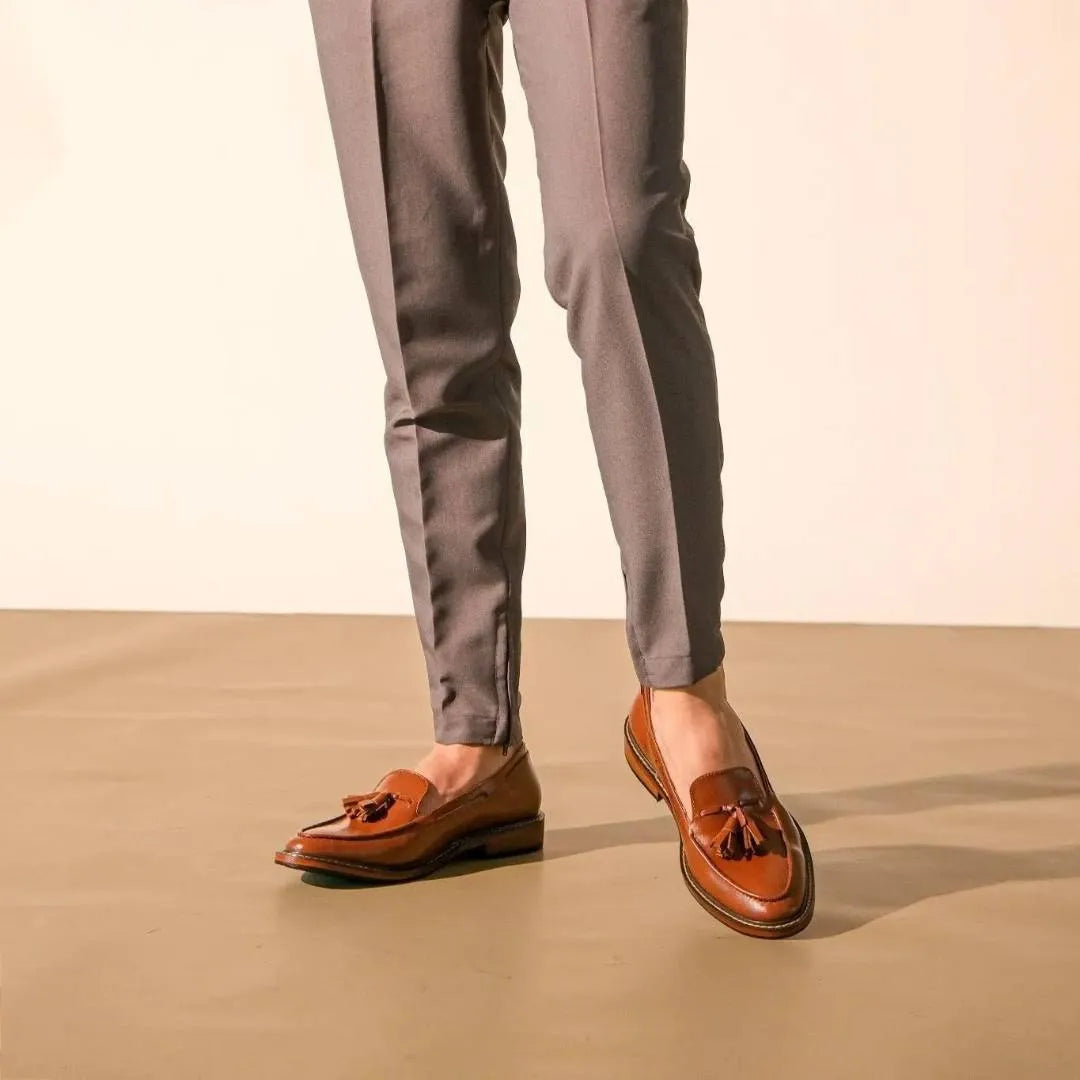 Brown loafers worn with gray pants on a beige background
#color_tan
