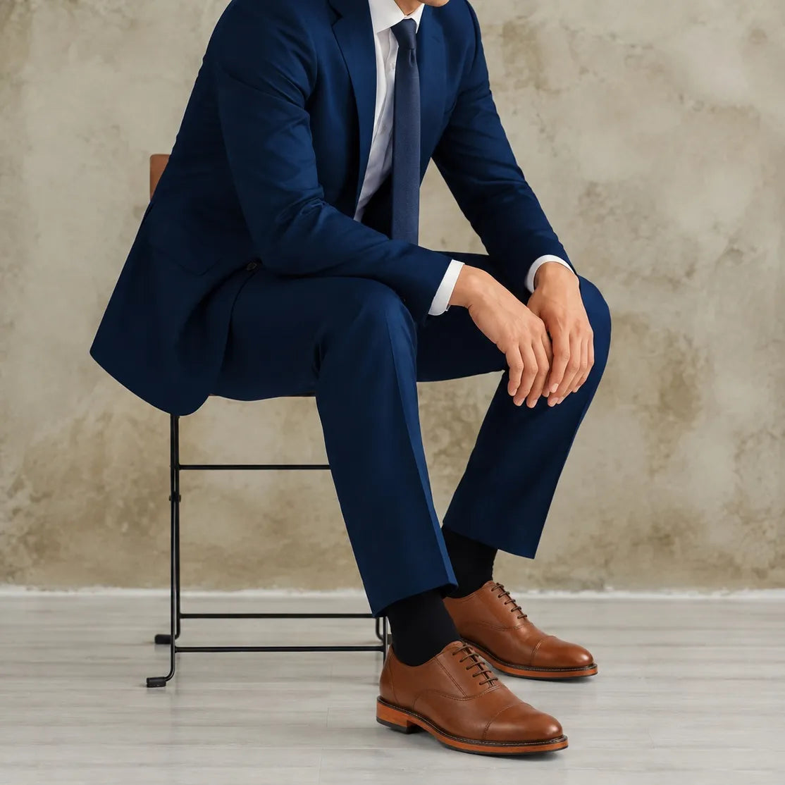 Man in a blue suit sitting on a stool against a textured wall.
#color_oxblood