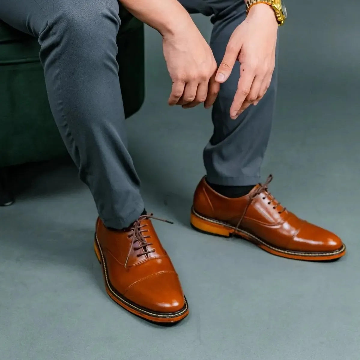 Person wearing tan brown leather shoes and gray pants against a gray background
#color_tan