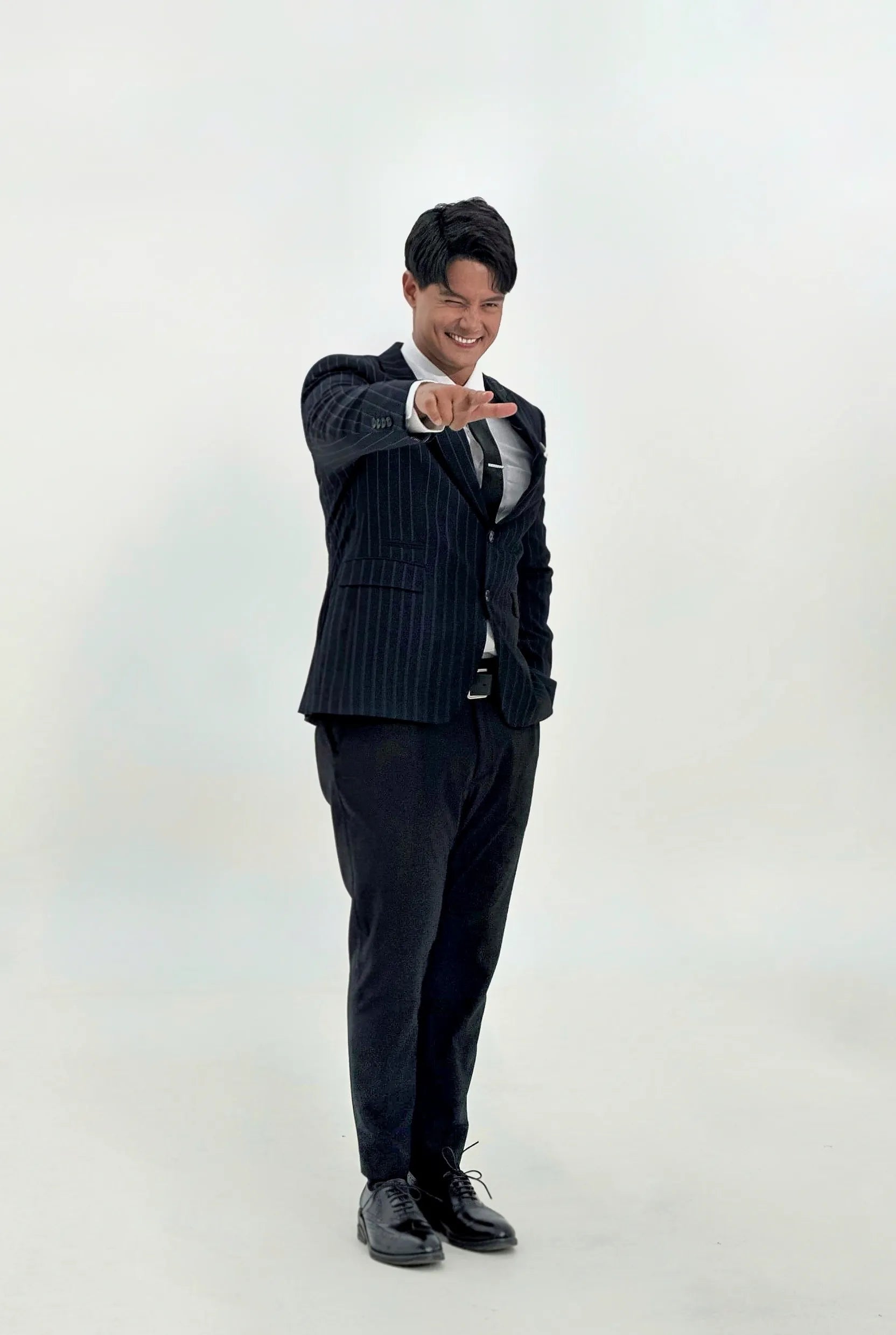 Daniel Matsunaga in a black suit wearing black wingtip oxford shoes posing against a white background
#color_black