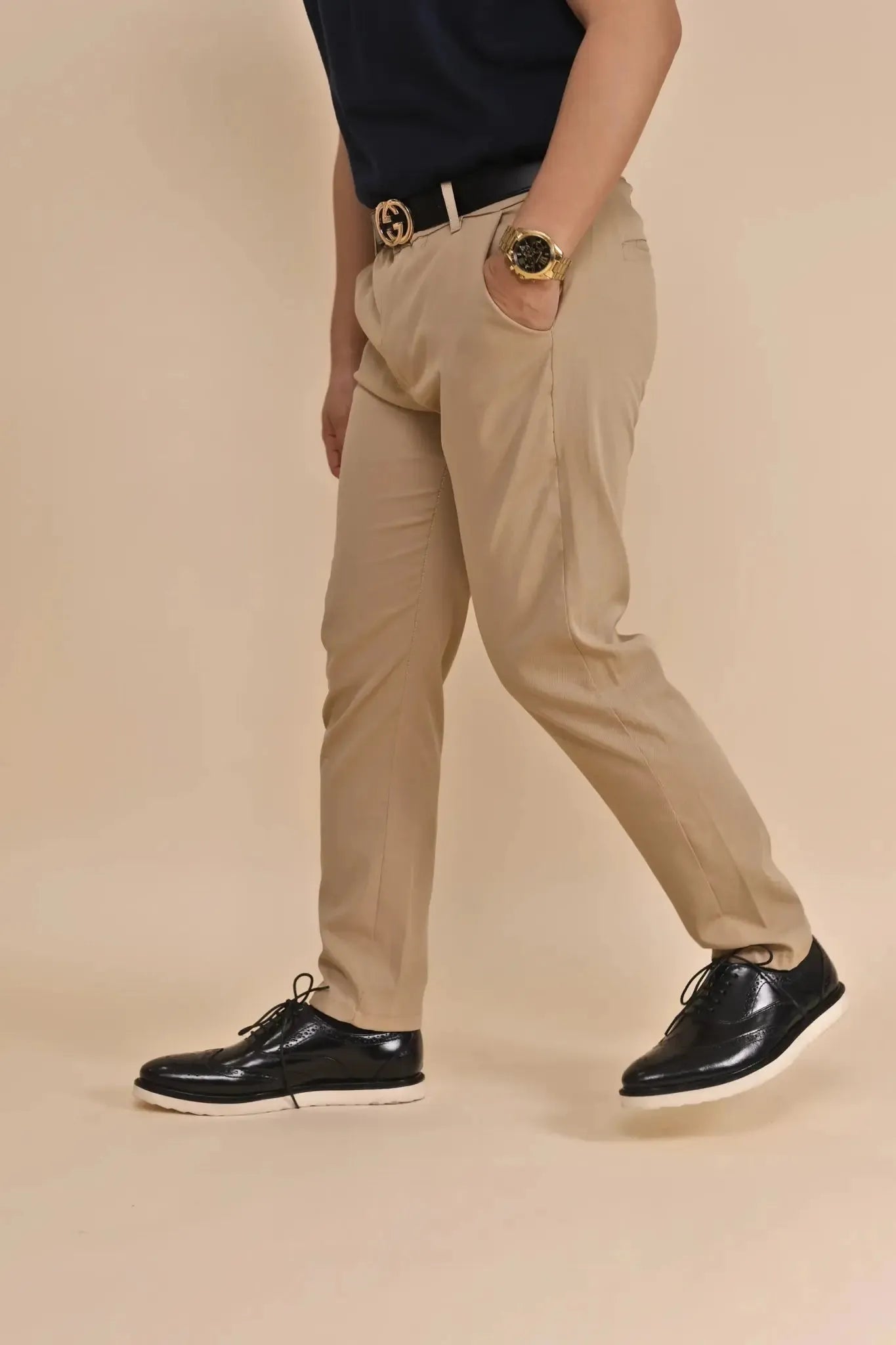 Person wearing beige pants, black leather wingtip shoes with rubber soles, and a navy shirt with a beige background
#color_black