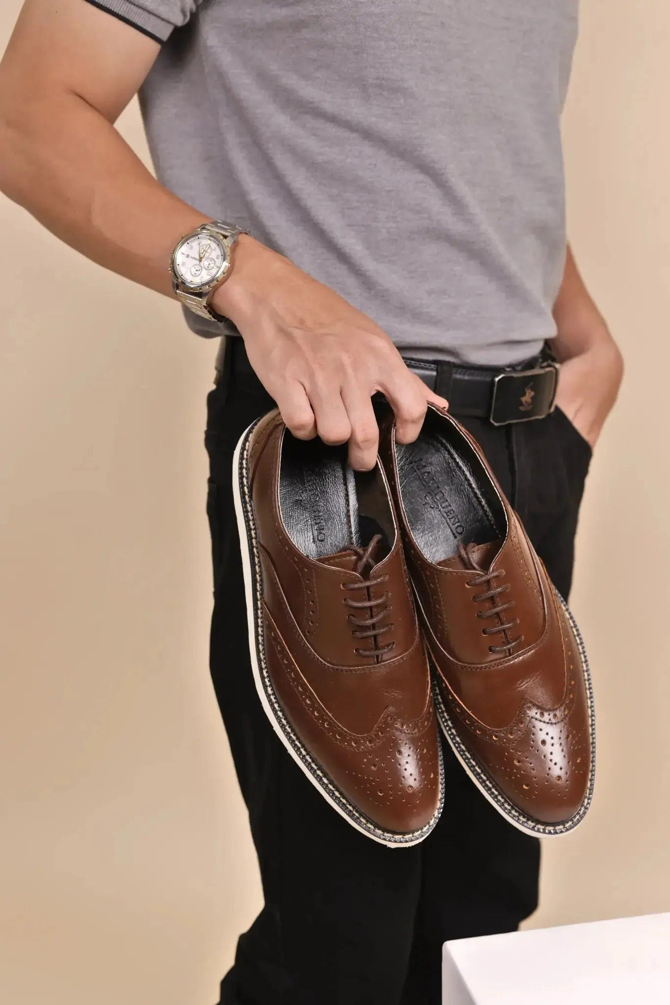 Person holding a pair of walnut brown wingtip rubber sole leather shoes against a beige background
#color_walnut