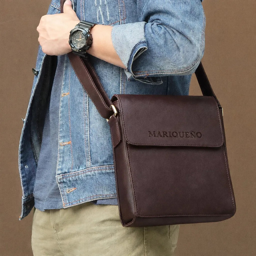 Person holding a walnut brown leather crossbody bag with 'MARIQUENO' branding against a brown background
#color_walnut