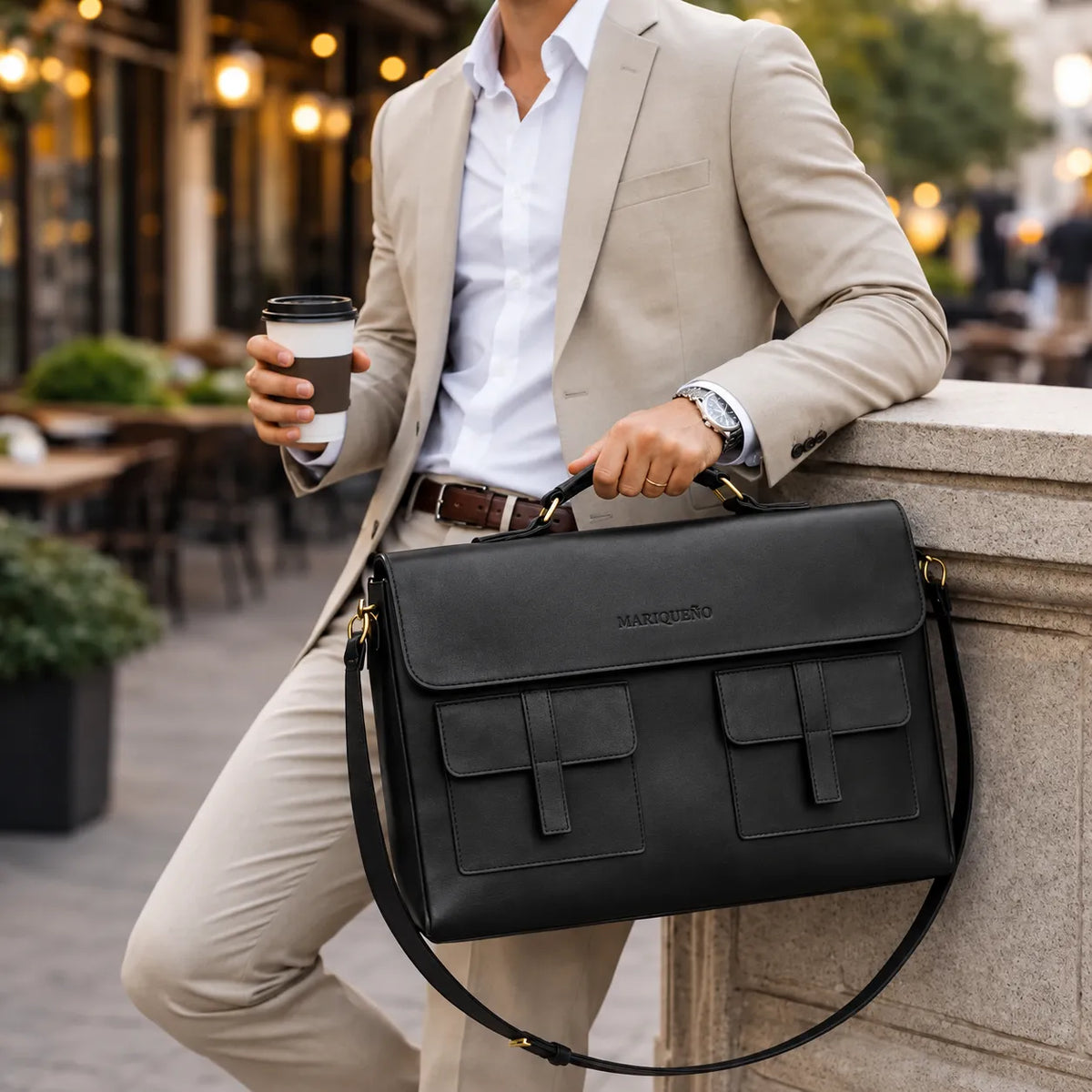 Man in a suit holding a black leather bag with 'Mariquéno' branding in an urban setting.
#color_black