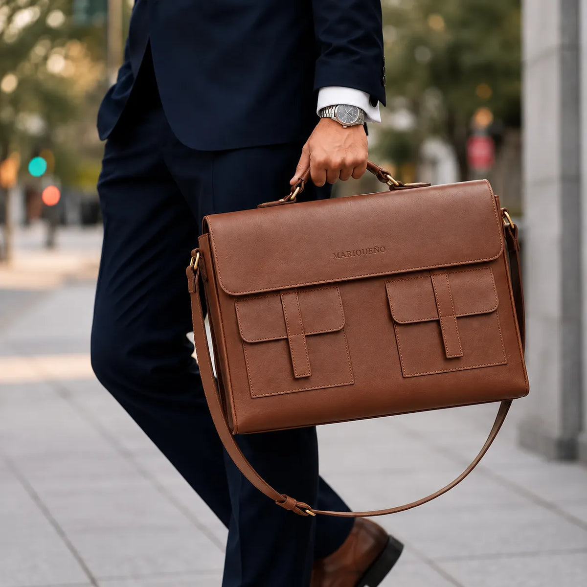 Person holding a brown leather briefcase with 'MARIQUENO' branding on a city street.
#color_walnut