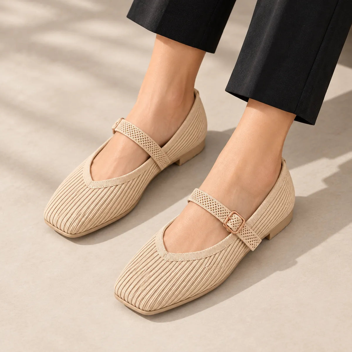 A person wearing black cropped pants and light beige Mary Jane flats with woven texture, captured mid-step against a soft beige studio background.
#color_beige