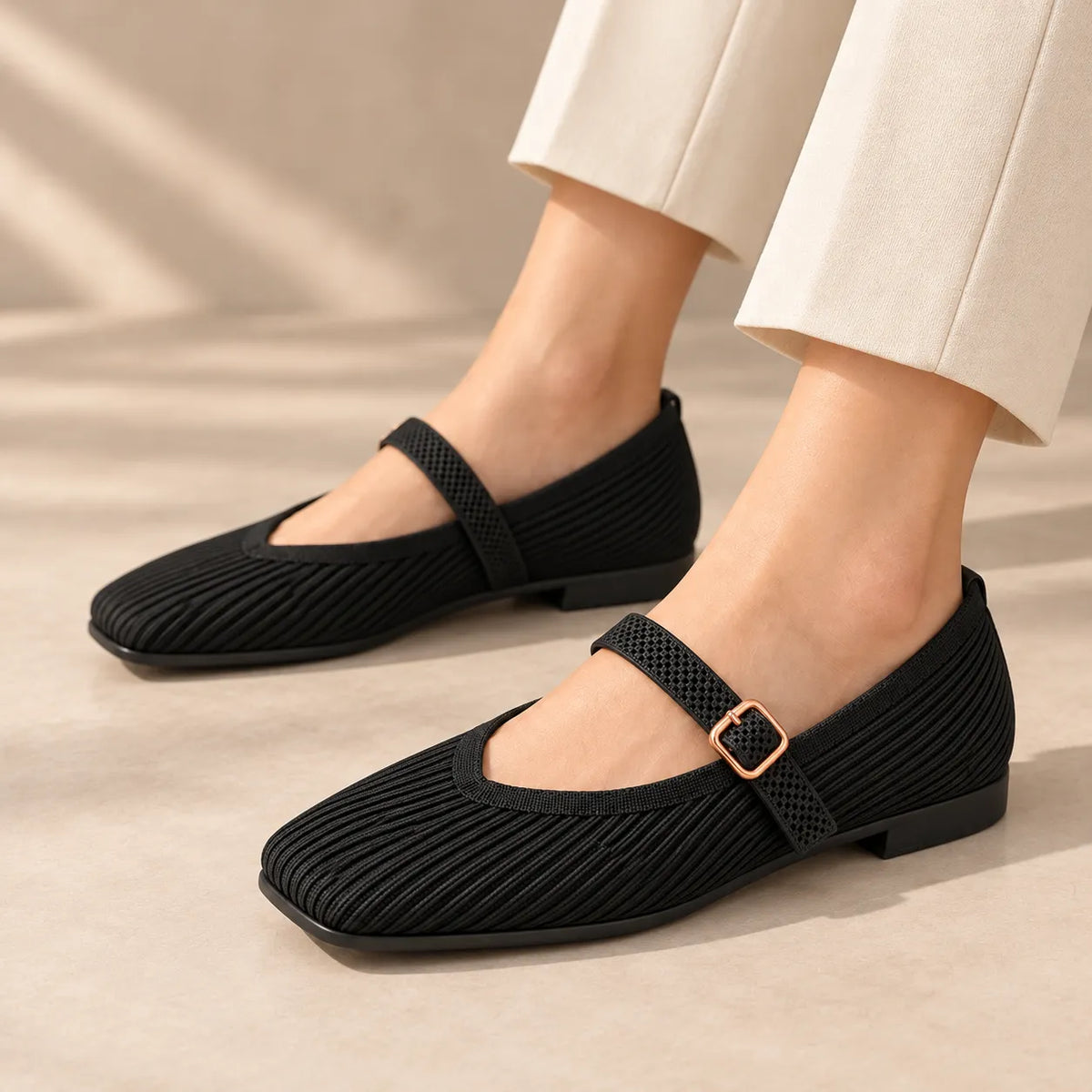 A person wearing beige cropped pants and black Mary Jane flat shoes, shown from the knees down against a soft light beige studio background.
#color_black
