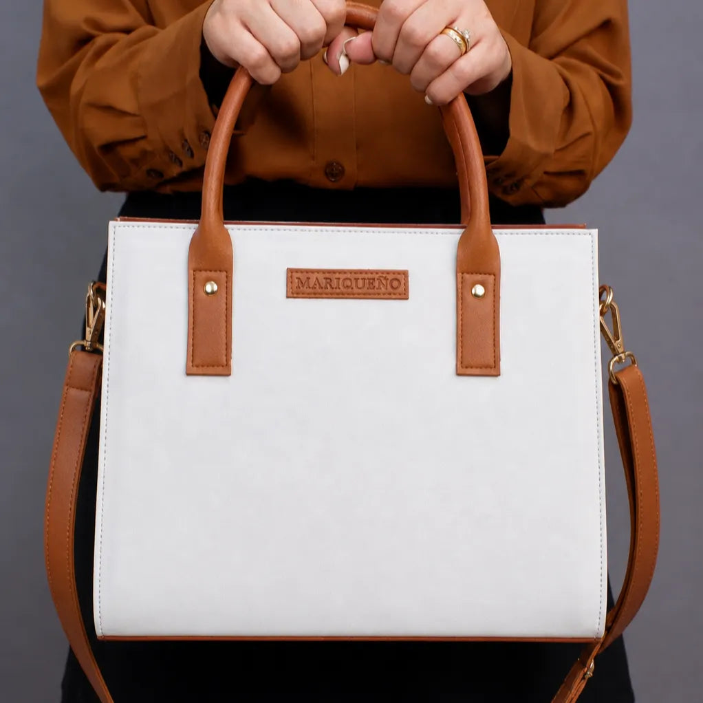 White handbag with brown handles and strap held by a person wearing a brown jacket.
#color_white