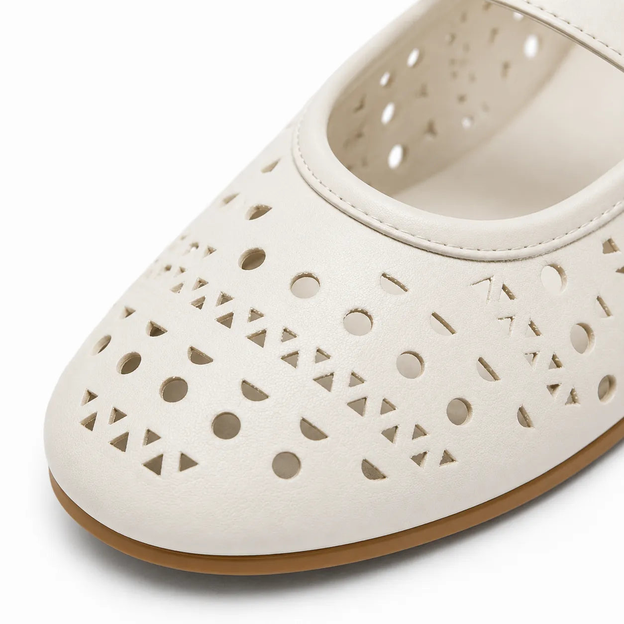 A close-up of a white perforated Mary Jane shoe with geometric cutouts and a tan sole, shown on a white background.
#color_white