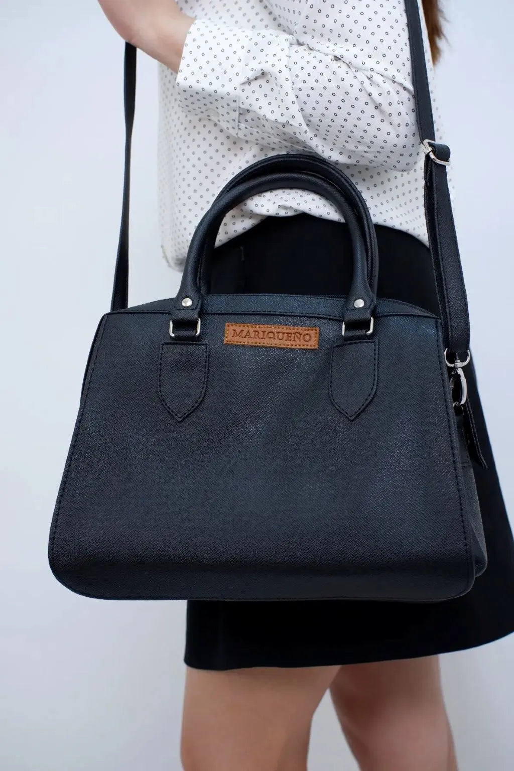 Black handbag with a visible brand logo held by a person against a plain background
#color_black