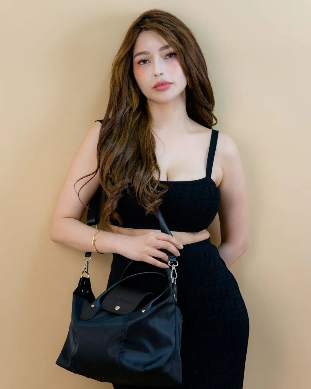 Woman holding a black handbag against a beige background
#color_black