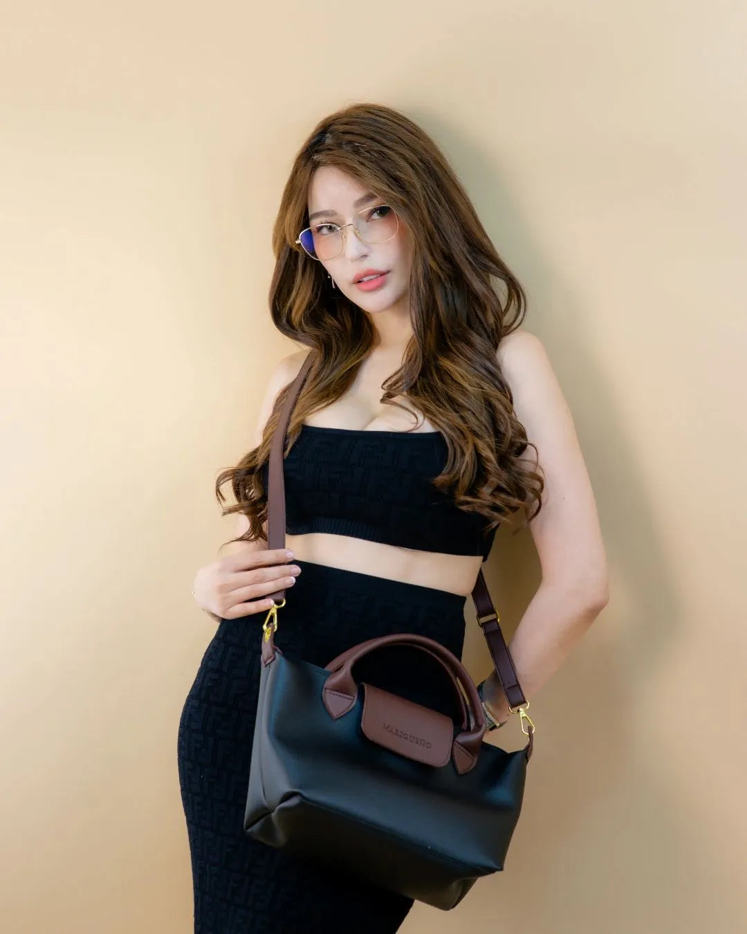 Woman holding a black handbag against a beige background
#color_black