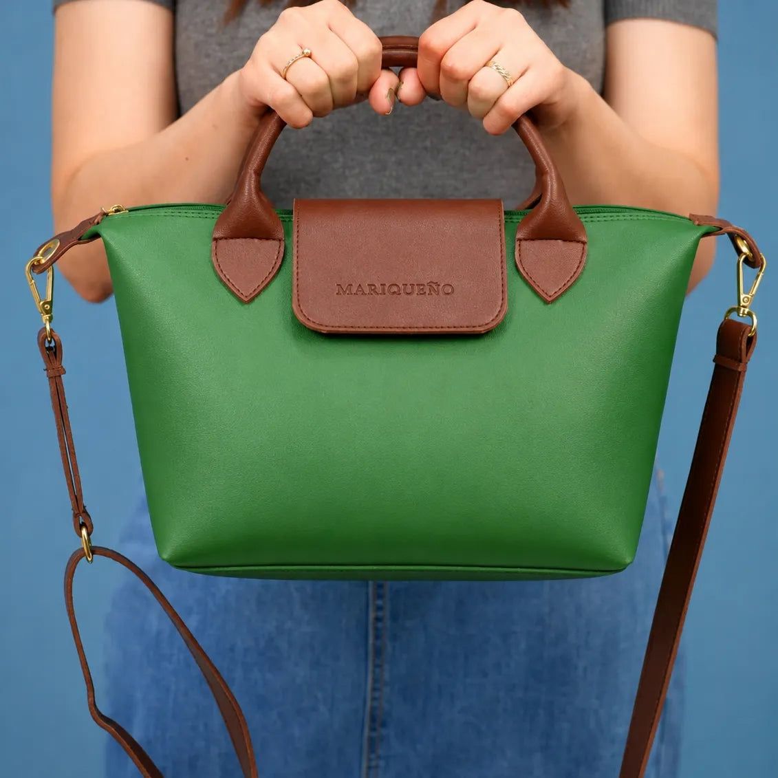 Green handbag with brown accents held by a person against a blue background
#color_emerald green