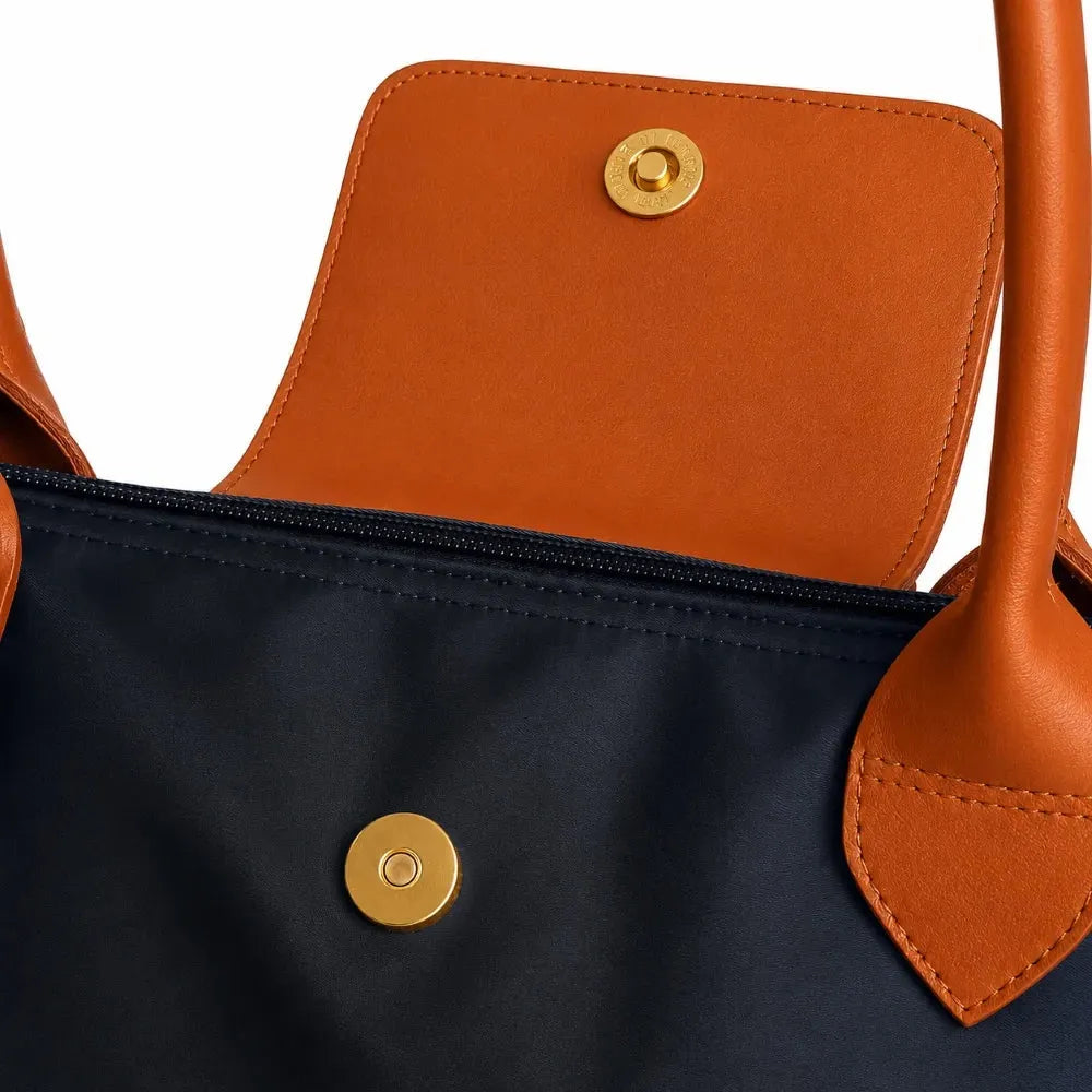 Close-up of a black bag with orange handles and trim, featuring a gold button.
#color_black and tan