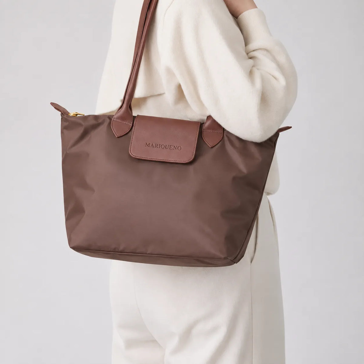 Brown handbag with leather accents held by a person wearing a white outfit on a light gray background
#color_choco brown