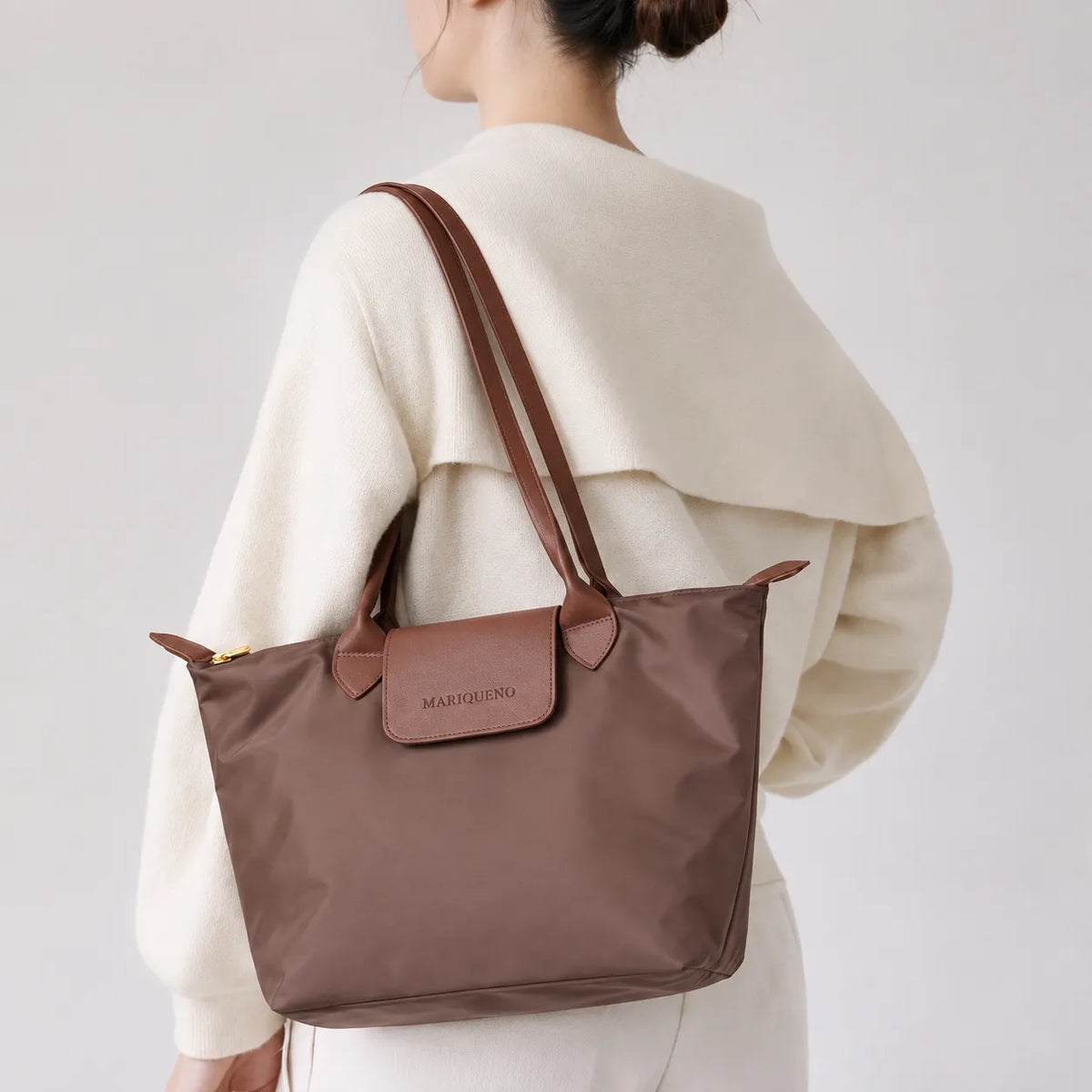 Person wearing a brown tote bag with a visible brand logo on a plain
background
#color_choco brown