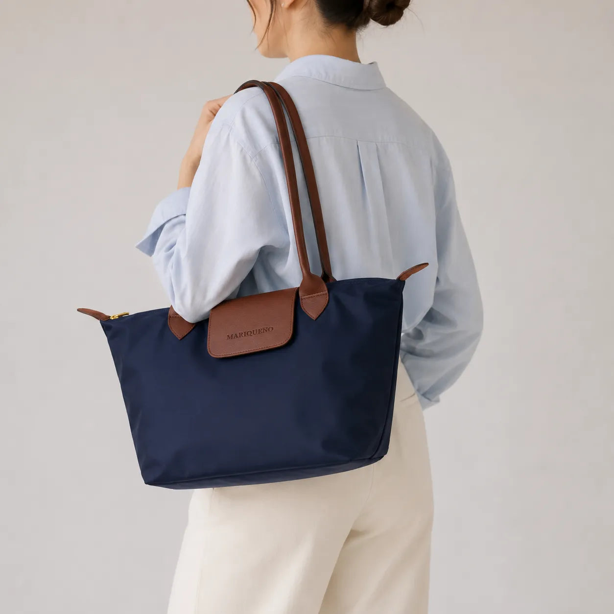 Person wearing a navy tote bag with brown leather accents on a plain background
#color_navy blue