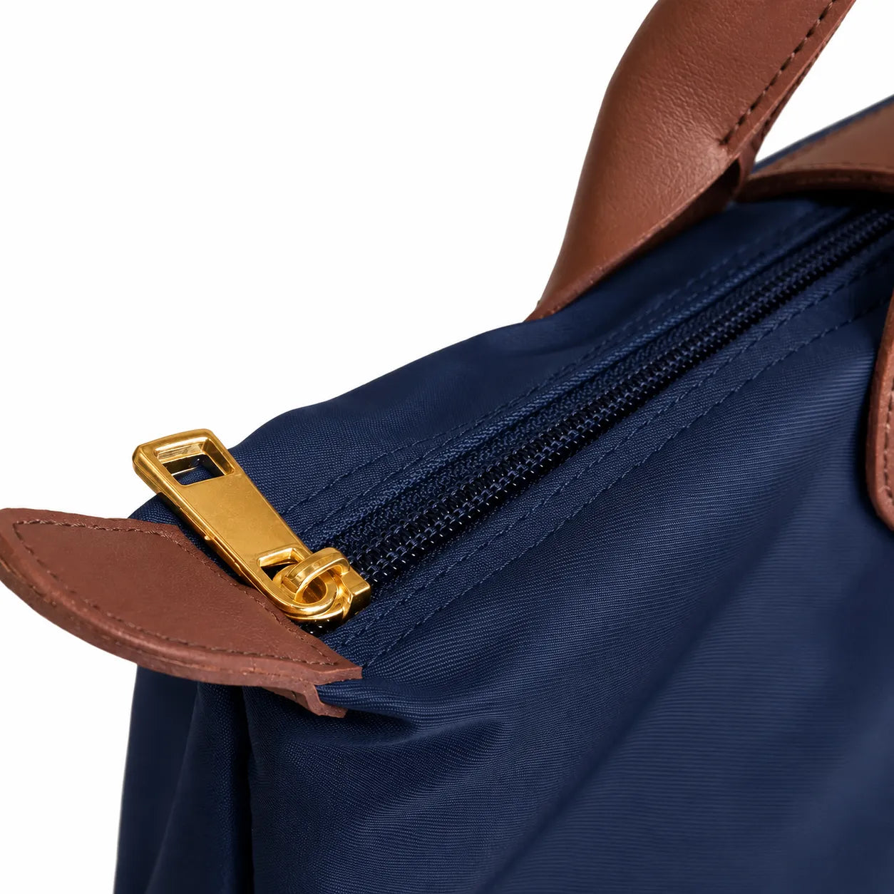 Close-up of a navy blue bag with a gold zipper and brown leather handle on a white background
#color_navy blue
