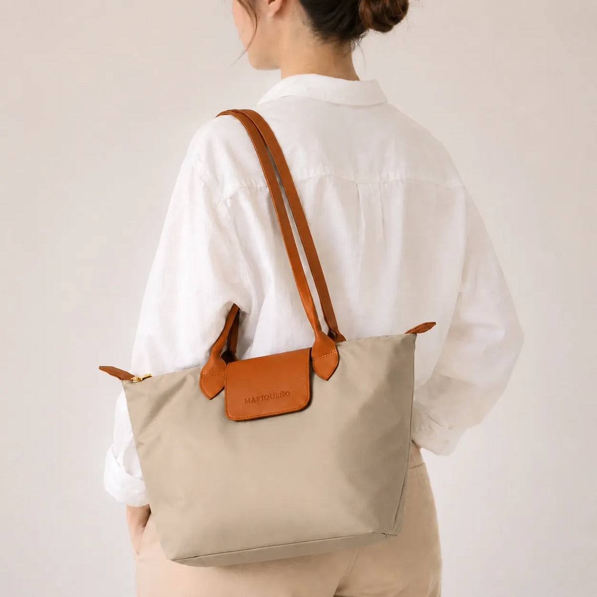 Taupe tote bag with brown leather accents held by a person against a gray background
#color_taupe