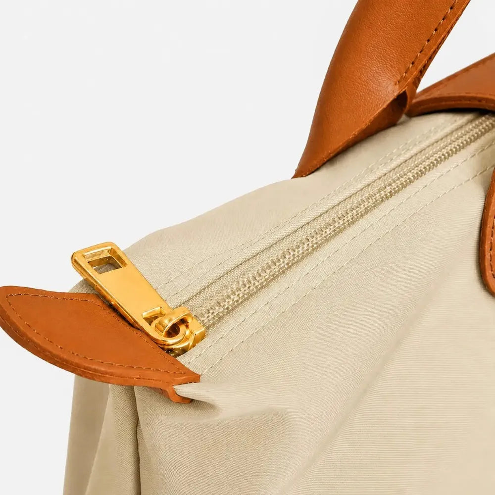 Close-up of a taupe bag with orange handles and zipper on a white background
#color_taupe