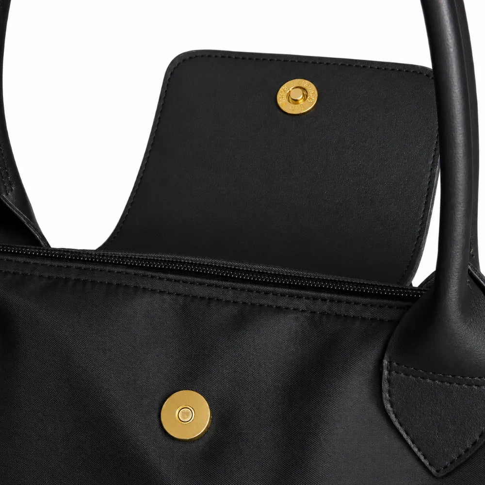 Close-up of a black nylon handbag showing the interior flap pocket with gold-tone snap buttons and a zipper.
#color_triple black