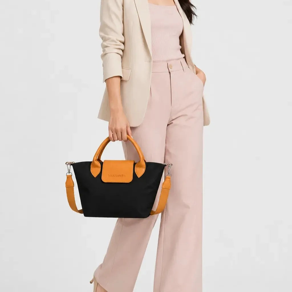 Person holding a black handbag with brown leather accents against a white background
#color_black and tan