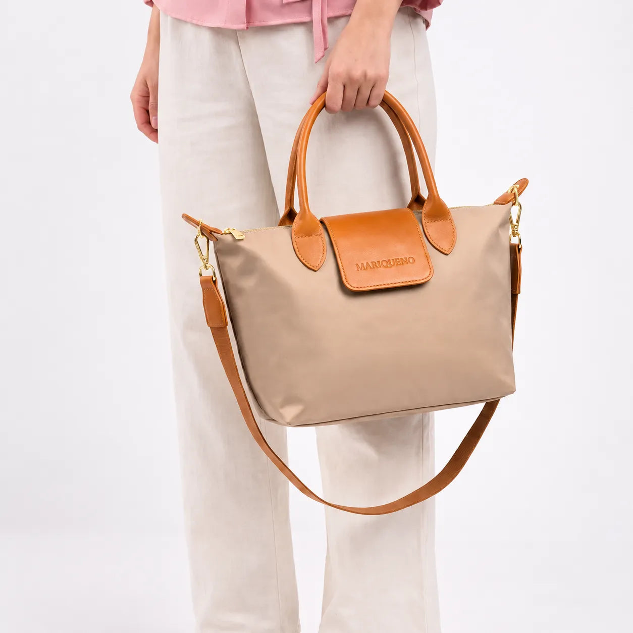 Beige handbag with brown handles and strap held by a person on a white background
#color_taupe