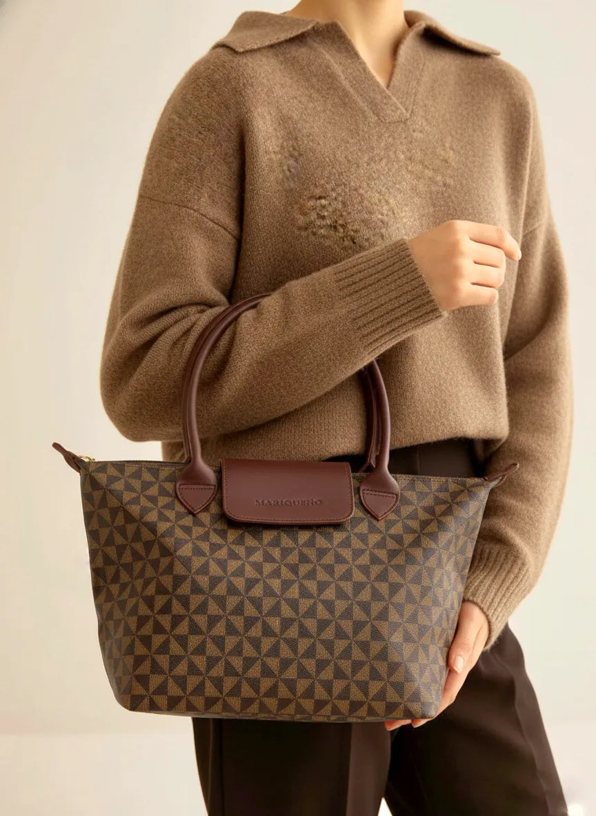 Person holding a brown patterned handbag with a plain background
#color_choco brown geo
