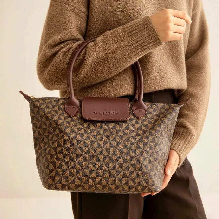 Person holding a brown patterned handbag with a plain background
#color_choco brown geo