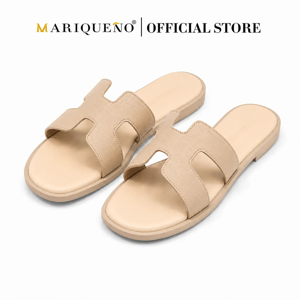 A pair of women's slide sandals in a light beige/tan color, featuring a wide cutout strap design. The sandals are displayed on a clean white background with a 'MARIQUEÑO | OFFICIAL STORE' logo overlay at the top.
#color_cream