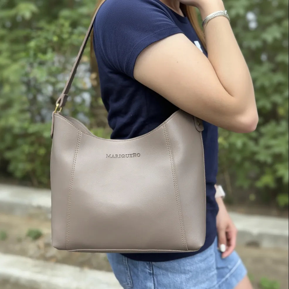 Person holding a taupe handbag with 'MARIQUENO' branding outdoors.
#color_taupe