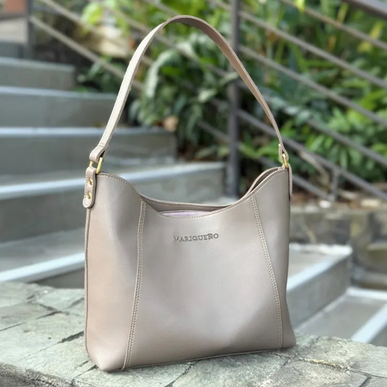 Taupe handbag with 'MARIQUENO' branding on a stone surface with greenery in the background
#color_taupe
