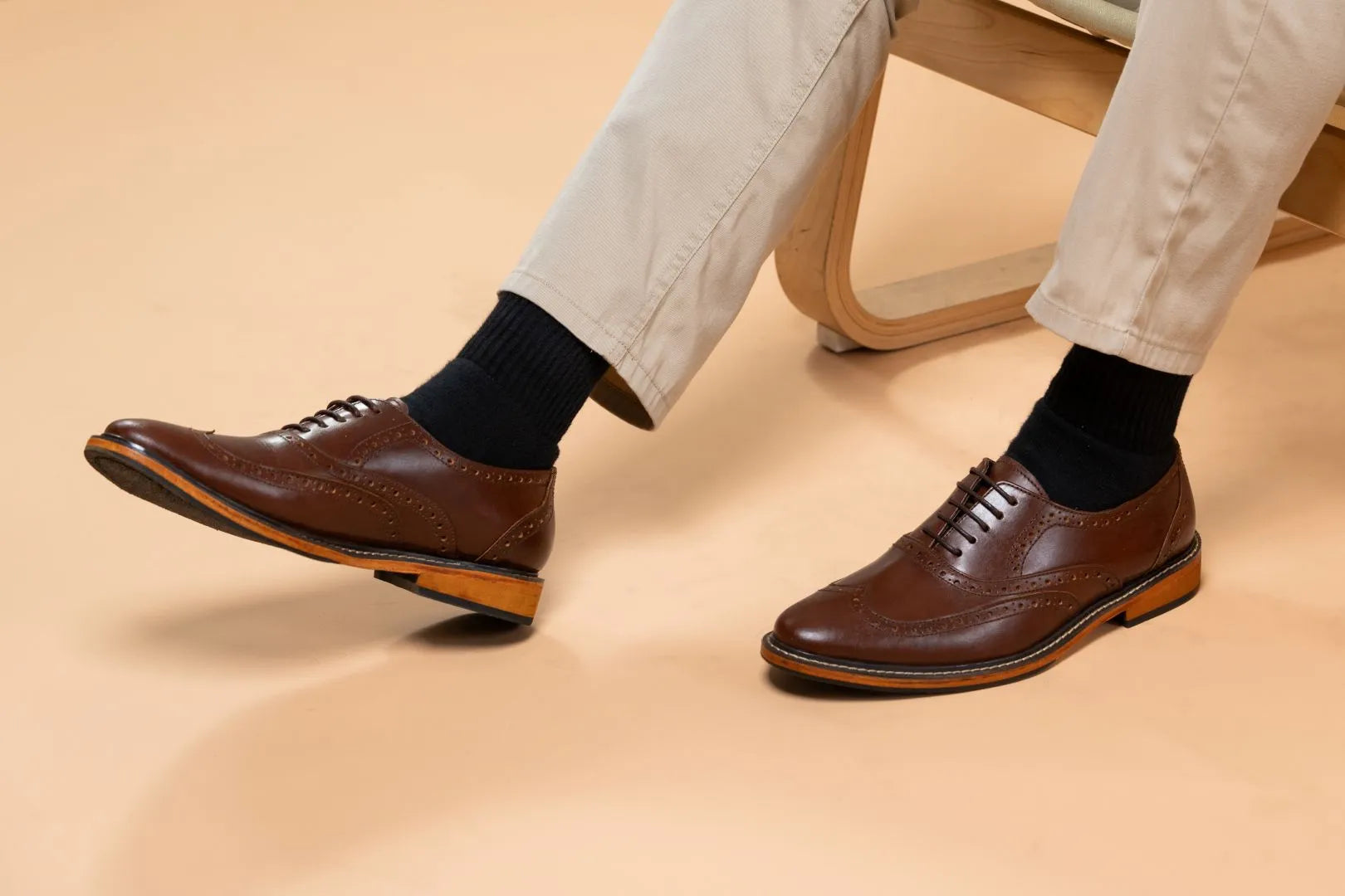 Brown dress shoes worn with beige pants on a beige background