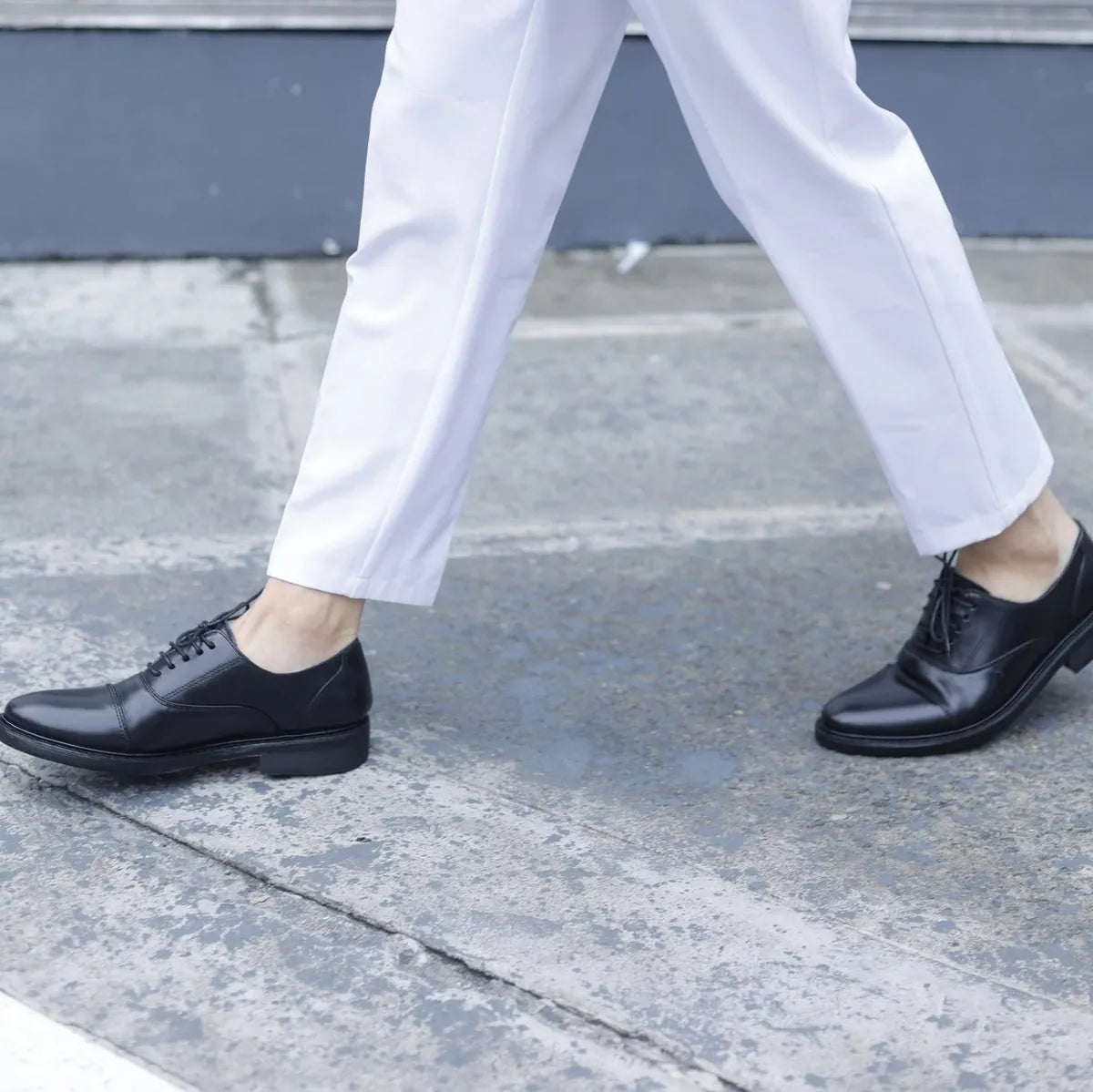 Person wearing white pants and black shoes on a sidewalk with a blurred background
#color_black