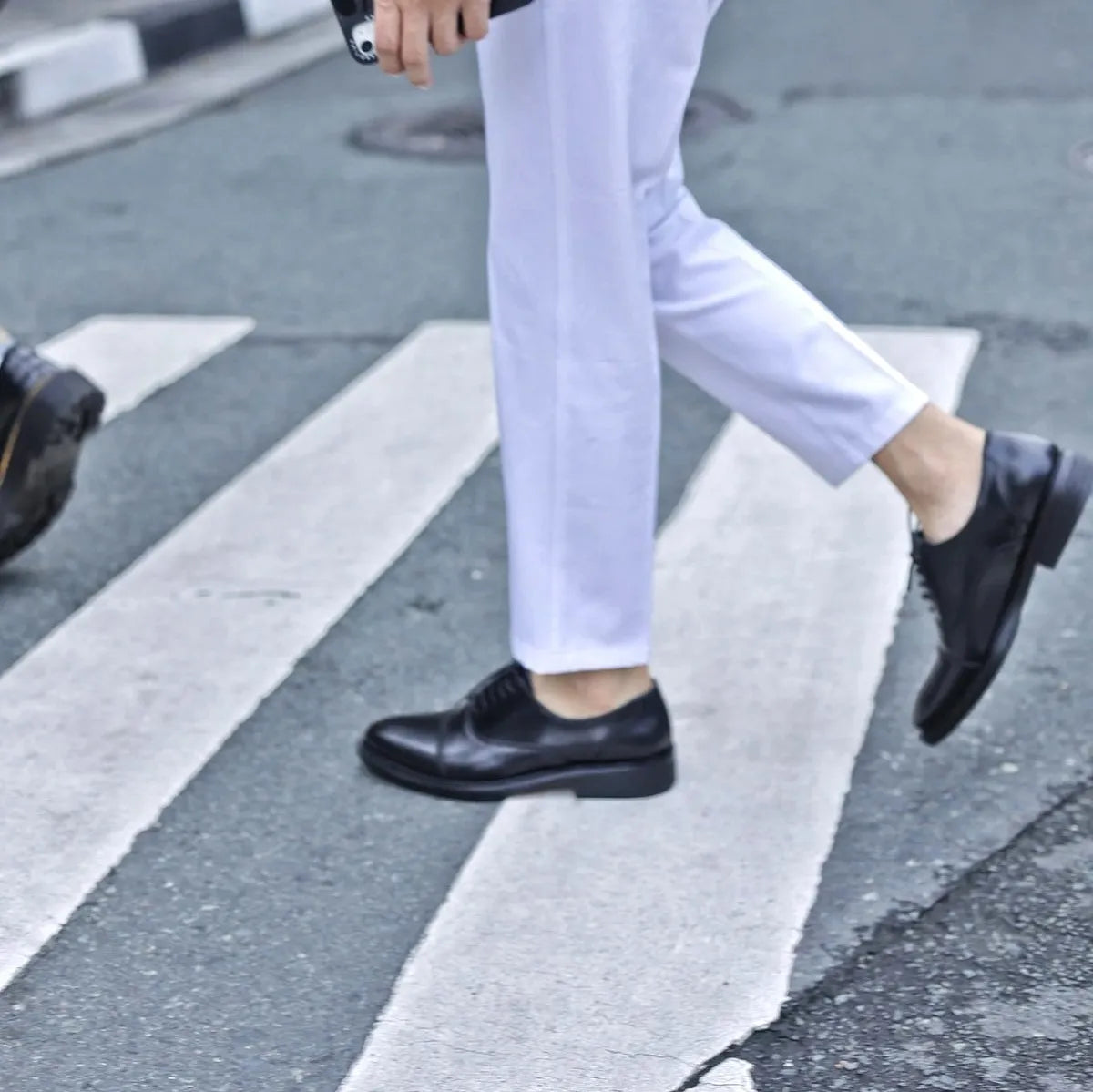 Person wearing white pants and black shoes crossing a street.
#color_black