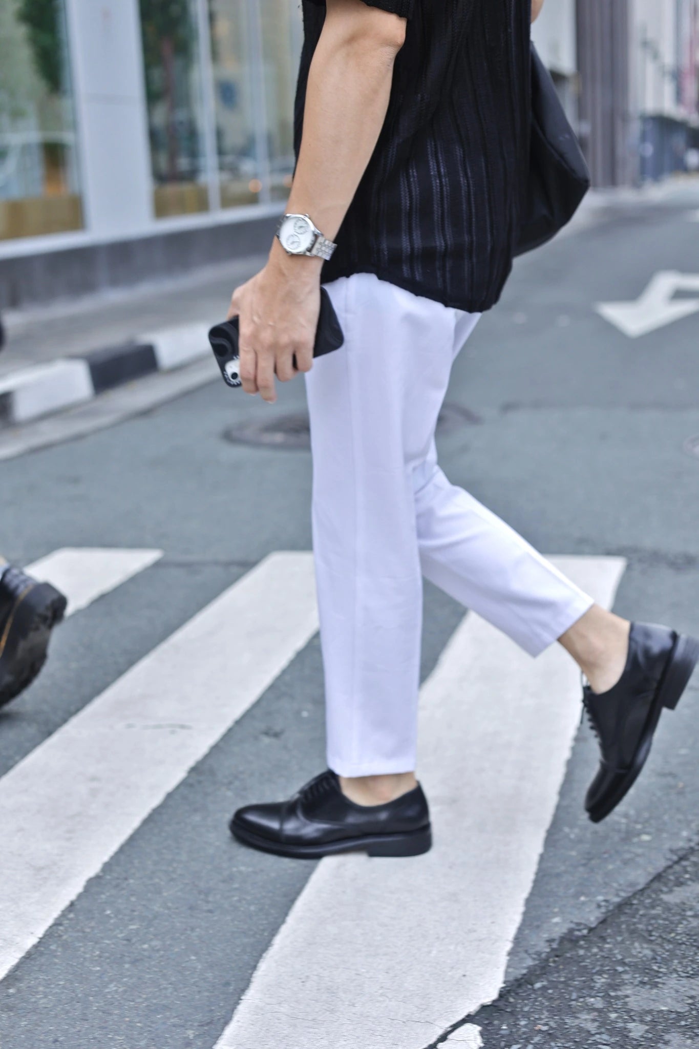 Person wearing white pants and black shoes crossing a street.
#color_black