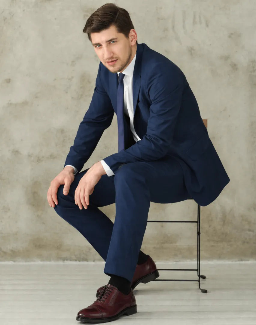 Man in a blue suit sitting on a stool against a textured wall.
#color_oxblood
