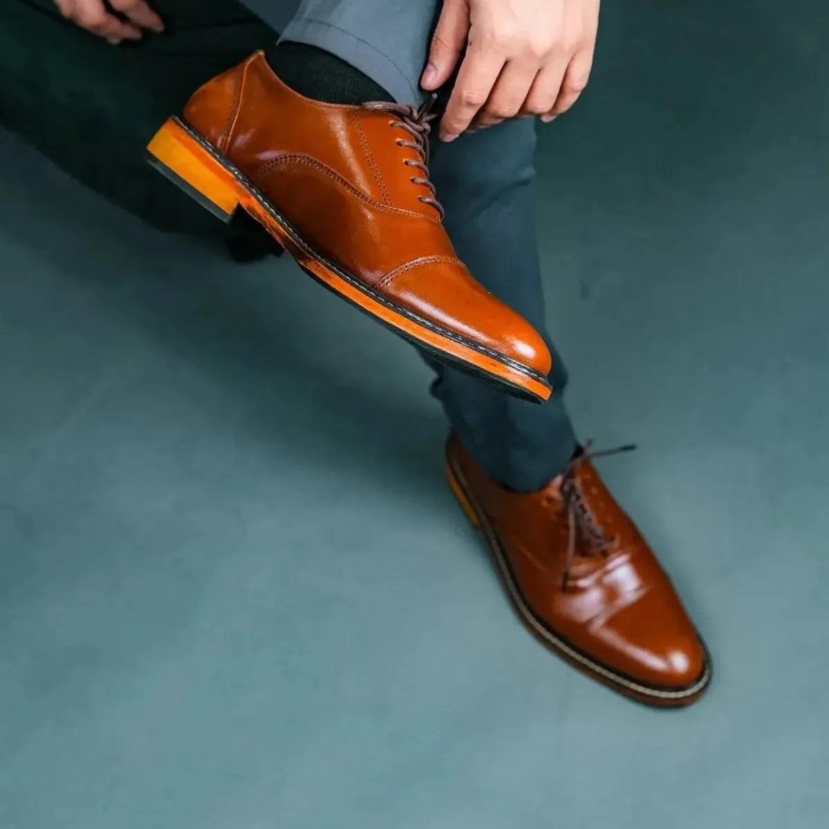 Person wearing brown dress shoes and gray pants on a gray floor.
#color_tan