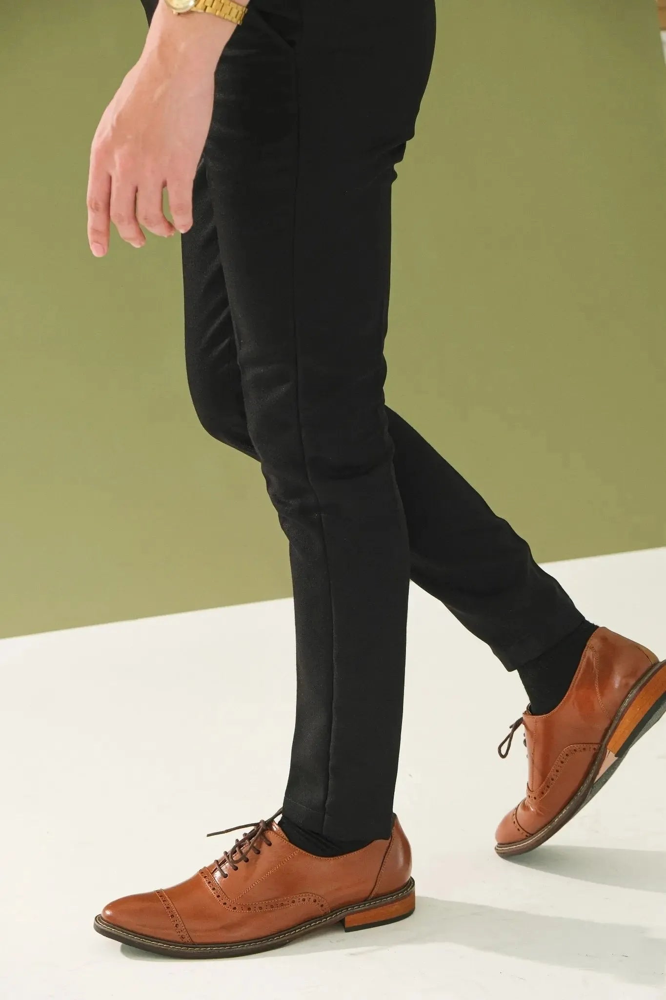 Person wearing black pants and tan brown leather shoes on a white surface with a green background
#color_tan