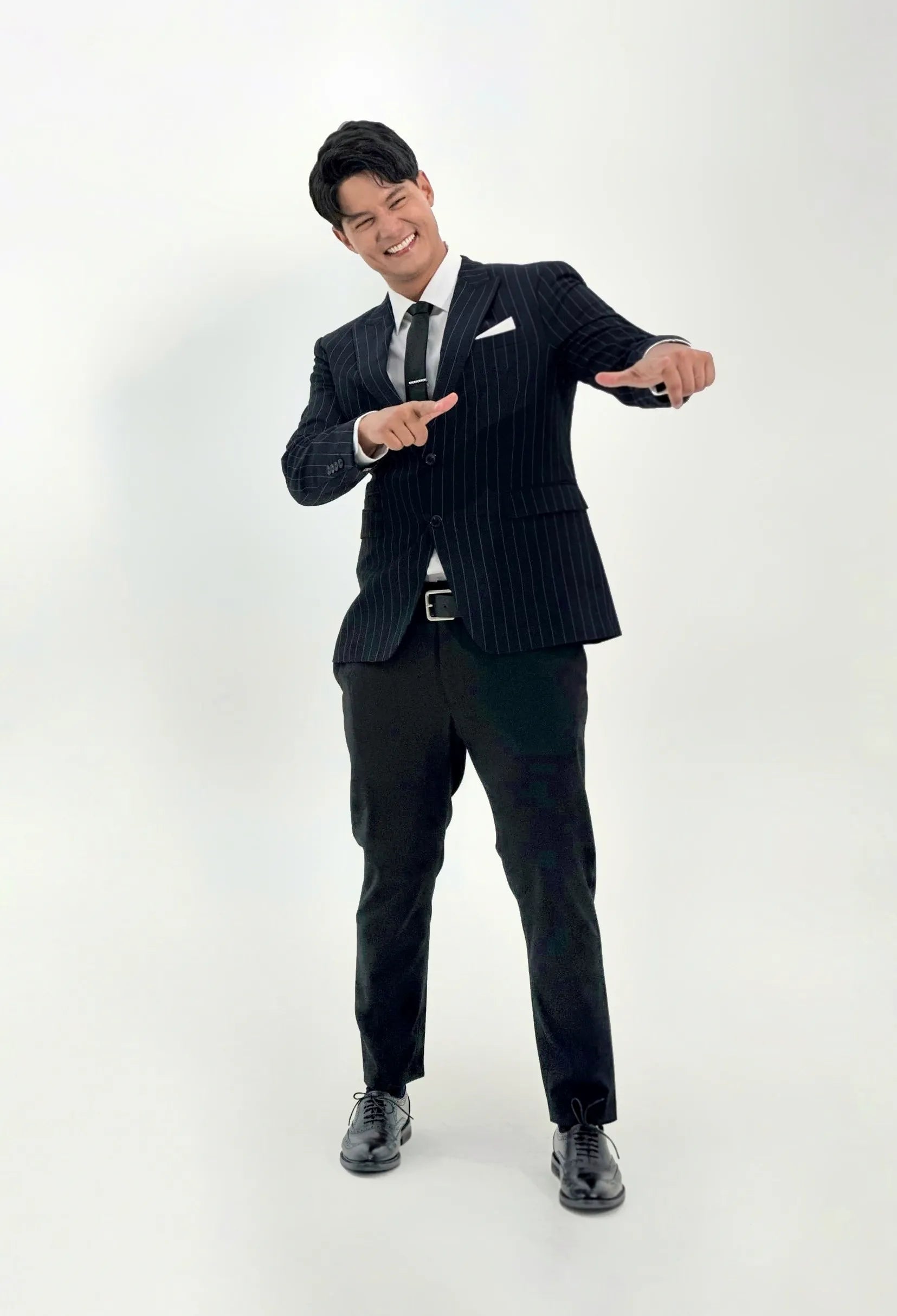 Daniel Matsunaga in a dark pinstripe suit posing against a white background wearing black wingtip oxford shoes
#color_black