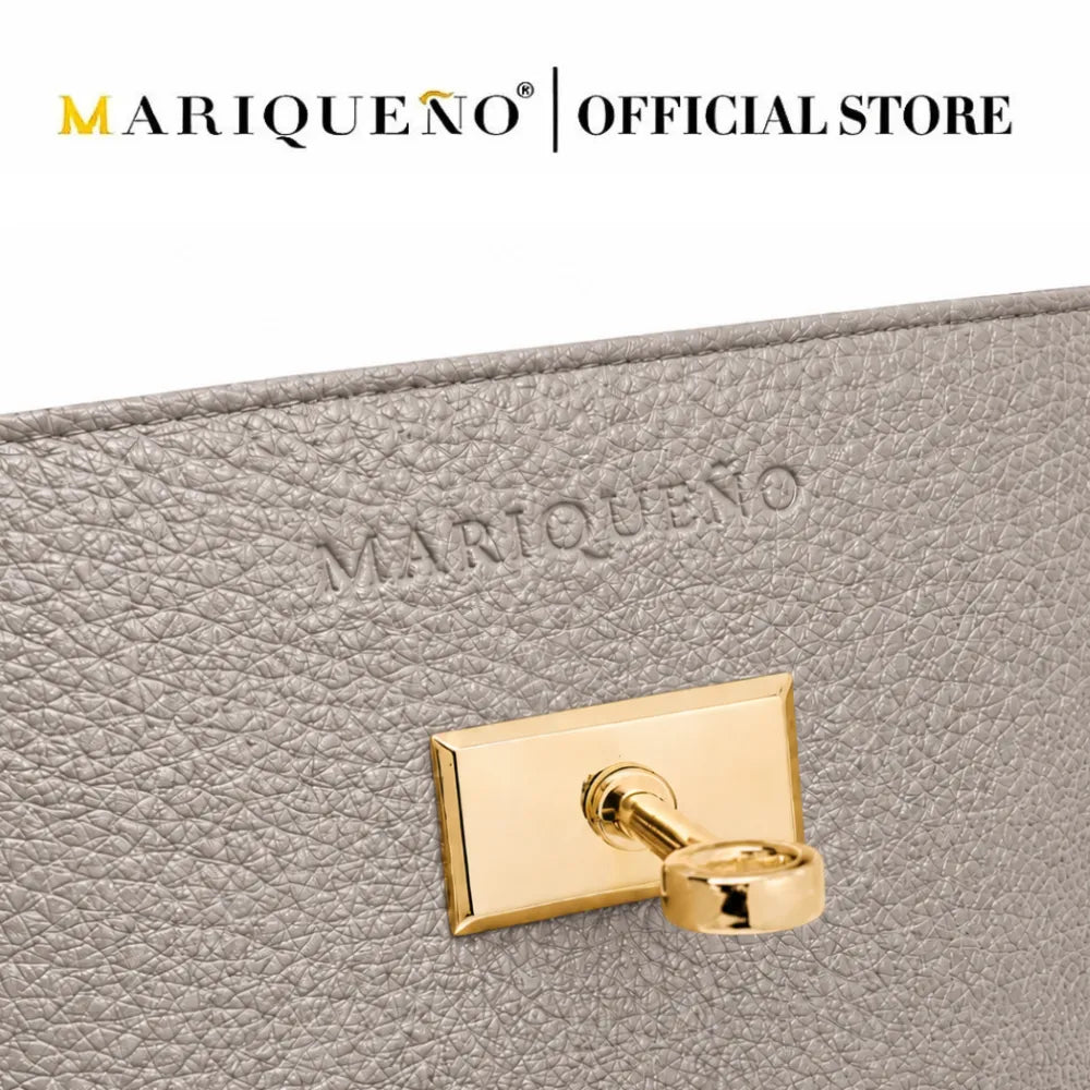 Close-up of a light gray textured leather clutch or wallet with an embossed MARIQUEÑO logo and a polished gold-tone metal clasp, shown against a white background with the MARIQUEÑO OFFICIAL STORE logo at the top.
#color_gray