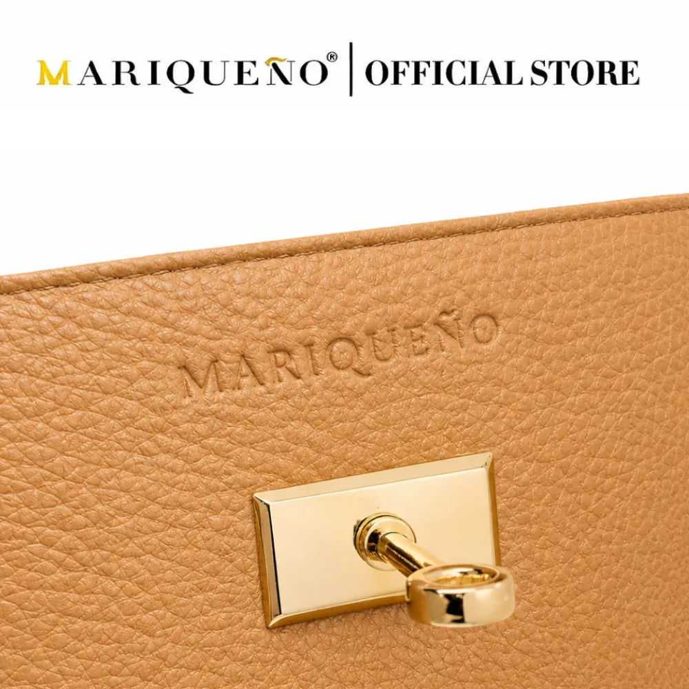 Close-up of a tan pebbled leather clutch or wallet with a gold-tone rectangular clasp and a key ring, featuring the embossed brand name 'MARIQUEÑO' on the leather. A white banner at the top reads 'MARIQUEÑO | OFFICIAL STORE'.
#color_tan