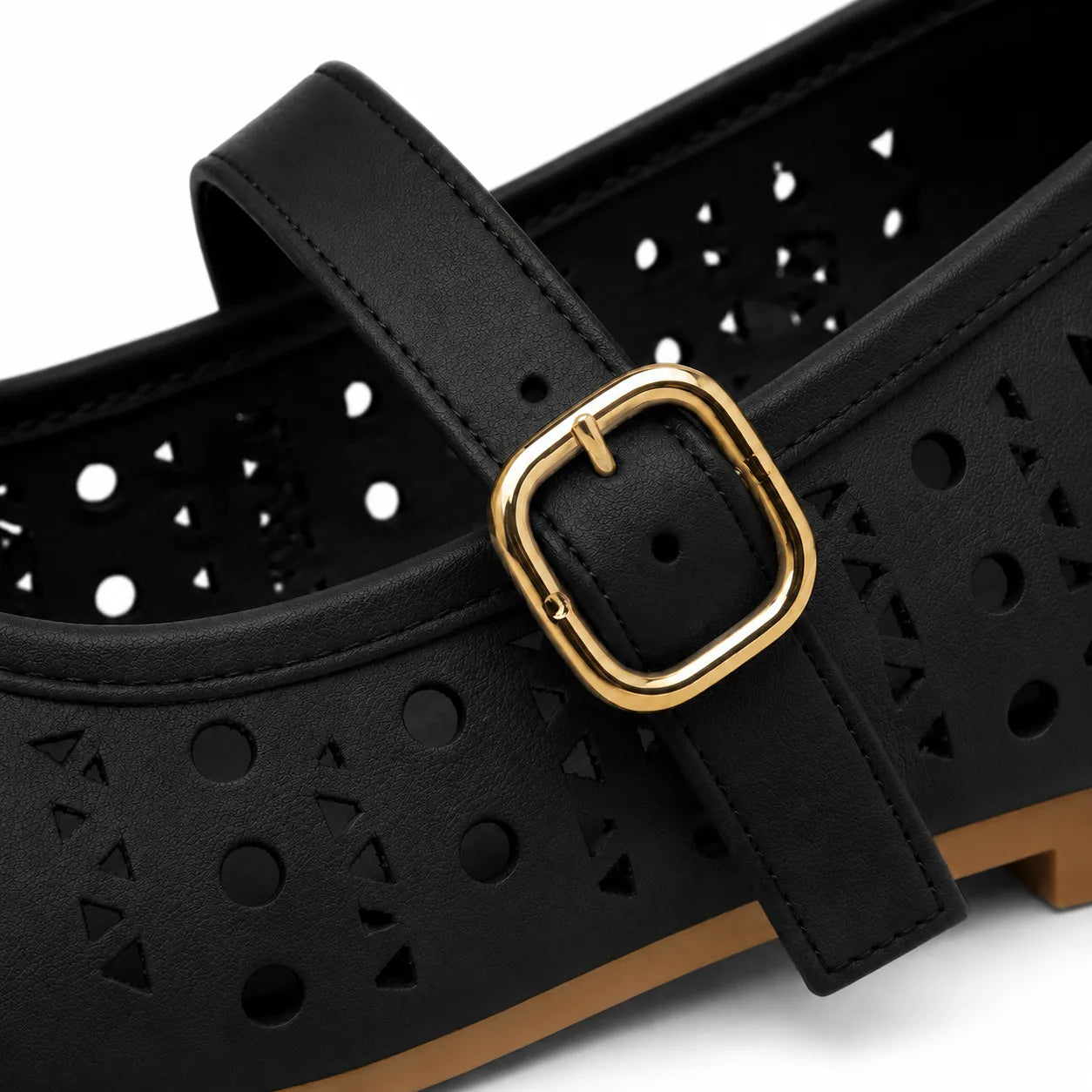 Close-up of a black perforated flat shoe with a gold buckle strap and a light brown sole, shown on a white background.
#color_black