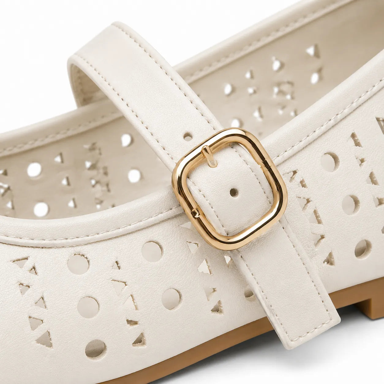 A close-up of a white faux-leather Mary Jane shoe featuring geometric laser-cut holes and a gold square buckle.
#color_white