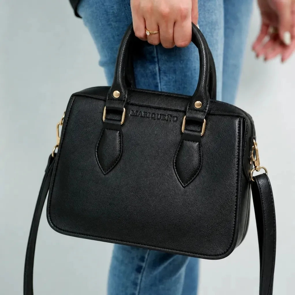 Black handbag with gold accents held by a person wearing blue jeans against a light gray background
#color_black