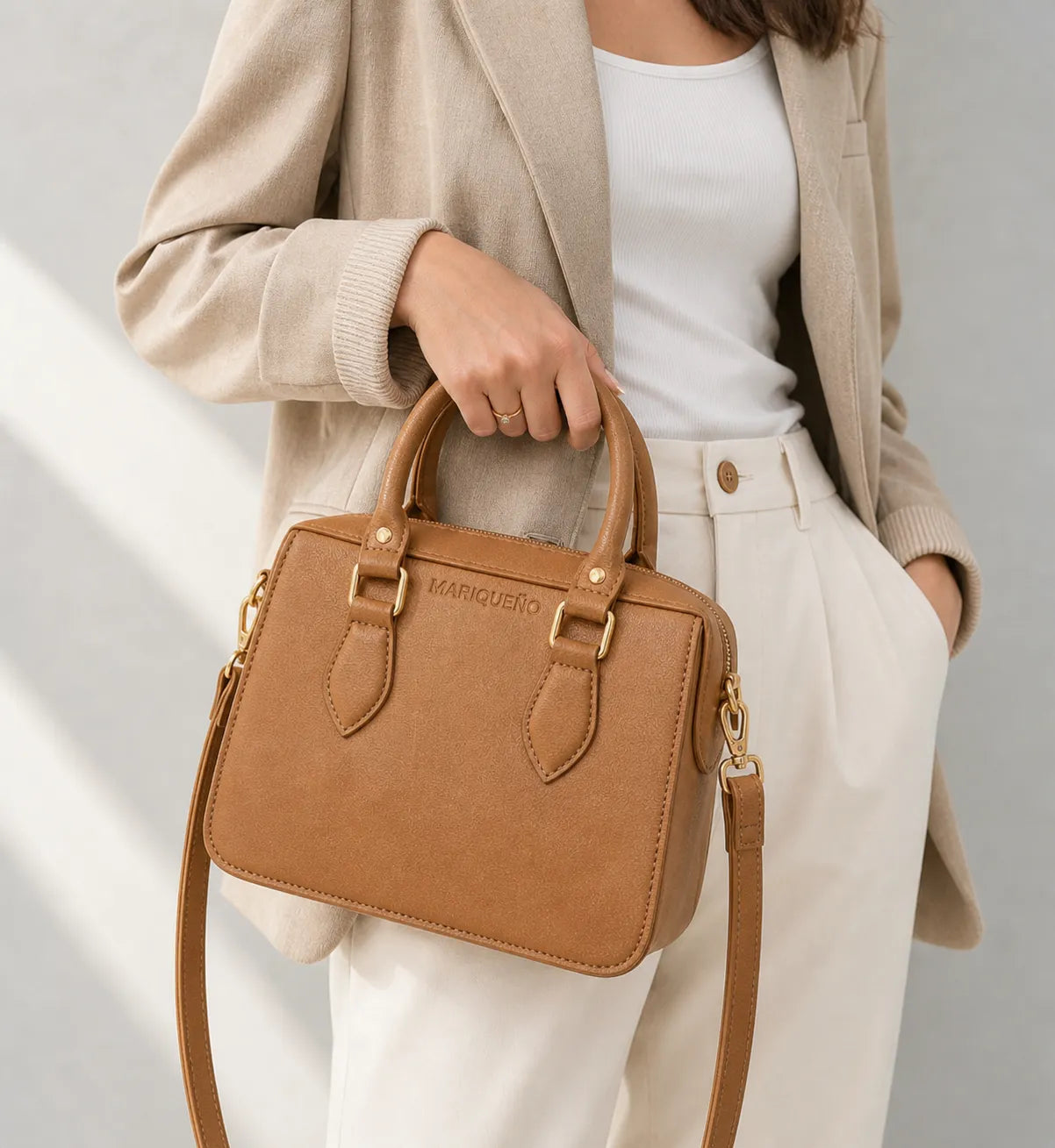 Person holding a brown handbag with a visible brand logo against a neutral background
#color_tan