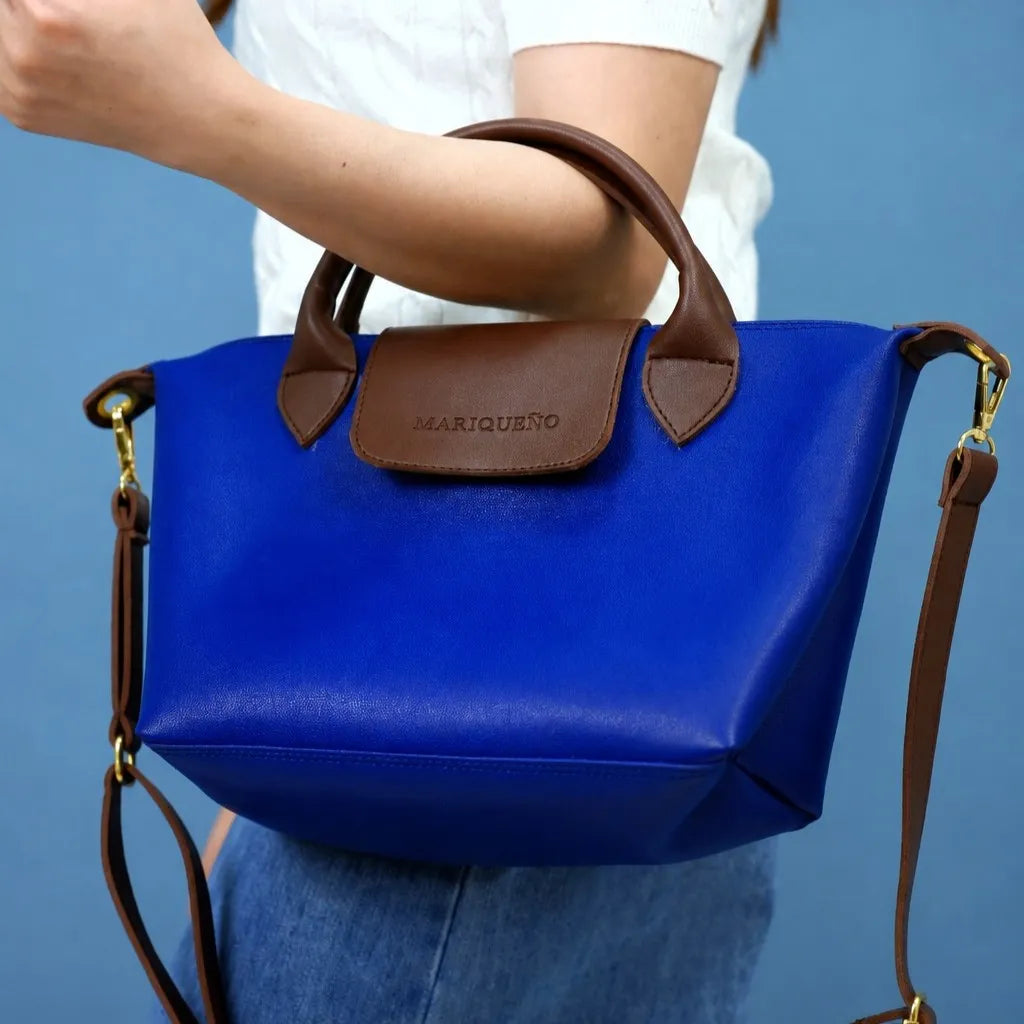 Blue handbag with brown handles and strap held by a person against a blue background
#color_royal blue