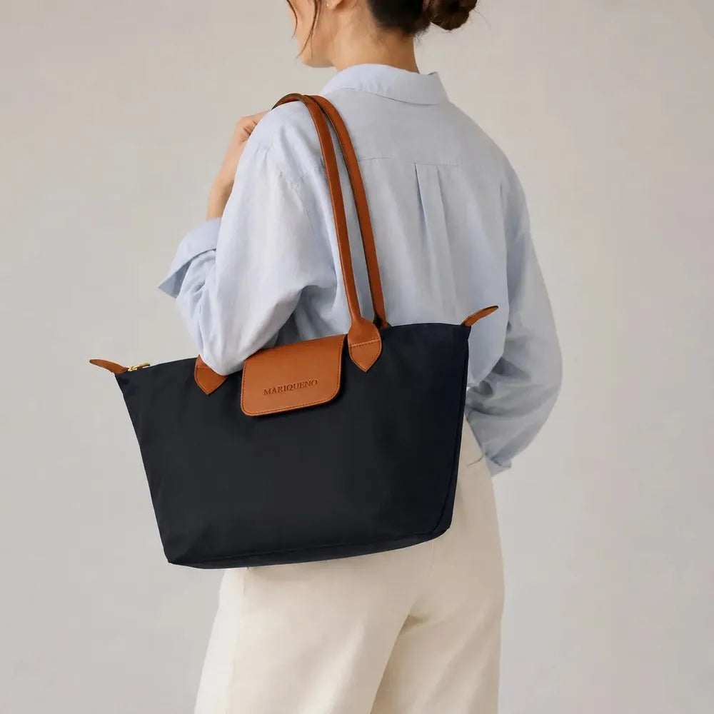 Person holding a black tote bag with brown handles and a visible brand label against a gray background
#color_black and tan